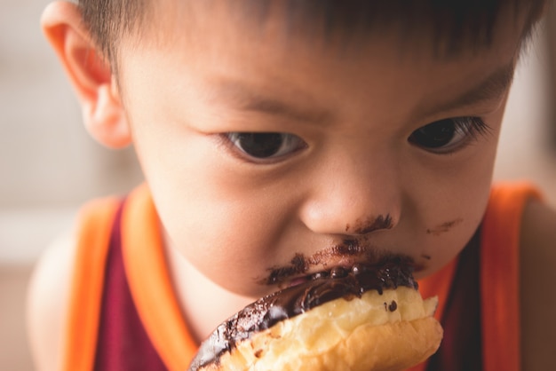 熱いドーナツを食べる空腹の小さな男の子の顔を閉じる