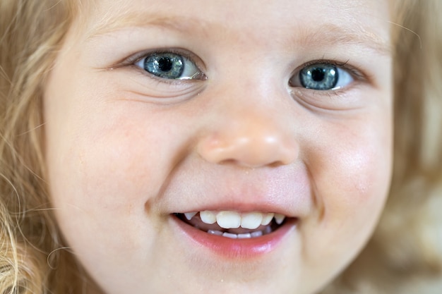 Бесплатное фото Закройте лицо маленькой милой девочки с большими голубыми глазами, улыбающейся девушкой.