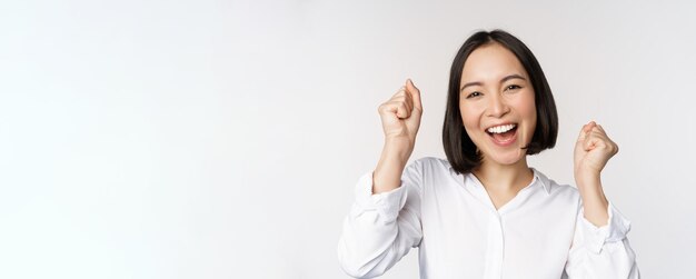 Close up face portrait of dancing asian woman smiling triumphing and celebrating with happy emotion standing over white background Copy space