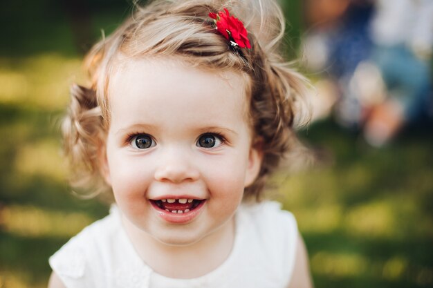 Close up of face of smiling beautiful baby girl on nature summer while posing at camera
