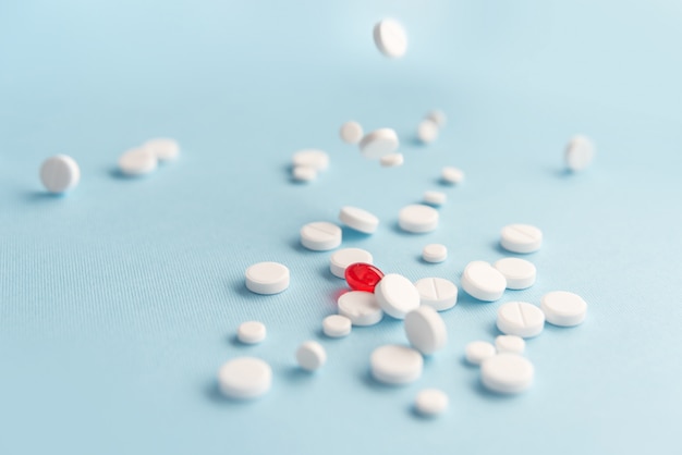 Close up of fallen white tablets with one red capsule