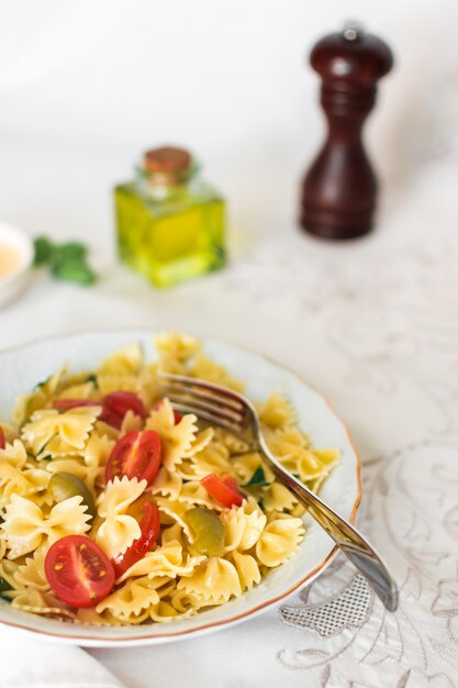 Close-up of farfalle pasta salad in white plate with fork on table cloth