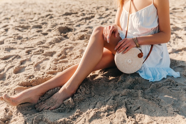 Крупным планом модные детали женщины в белом платье с соломенной сумочкой в летнем стиле на пляжных аксессуарах
