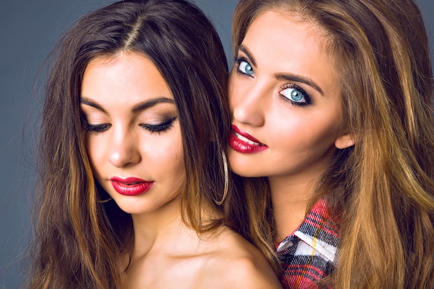Close up fashion portrait of amazing blonde and brunette woman, perfect skin, bright make up, pure beauty, full sexy red lips, autumn winter style ,