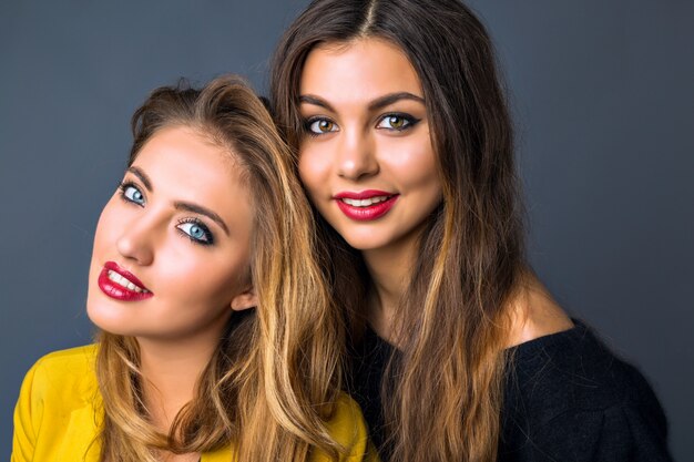 Close up fashion portrait of amazing blonde and brunette woman, perfect skin, bright make up, pure beauty, full sexy red lips, autumn winter style ,