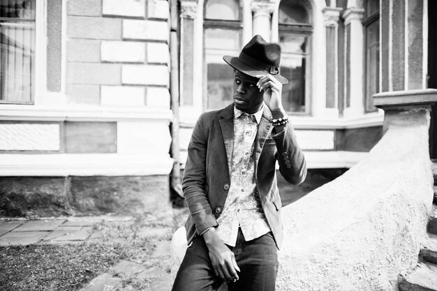 Close up fashion portrait of black african american man on green velvet jacket and black hat sit on stairs background old mansion BW photo