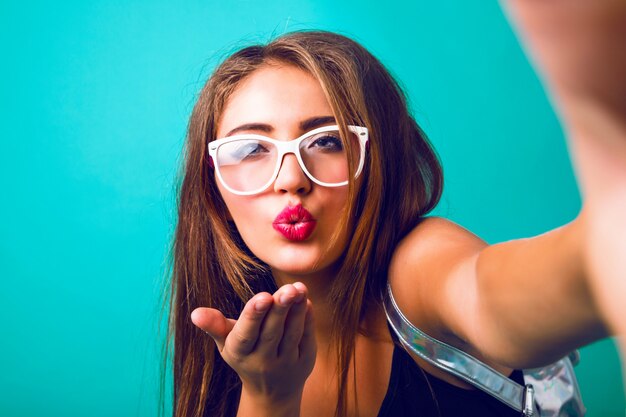 Close up fashion portrait of hipster woman with vintage sunglasses blowing air kiss