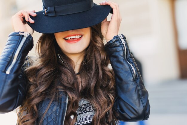 Close up fashion portrait of pretty seductive young woman with wool hat smiling, laughing, posing outdoor. Red lips, wavy hairstyle.