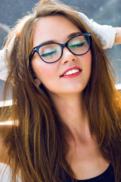 Close up fashion  portrait of young sexy stunning sensual woman with long brunette hairs perfect skin and bright makeup, wearing clear hipster vintage glasses.