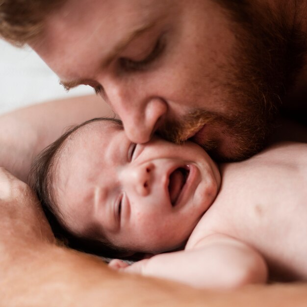 Close-up father kissing moody baby