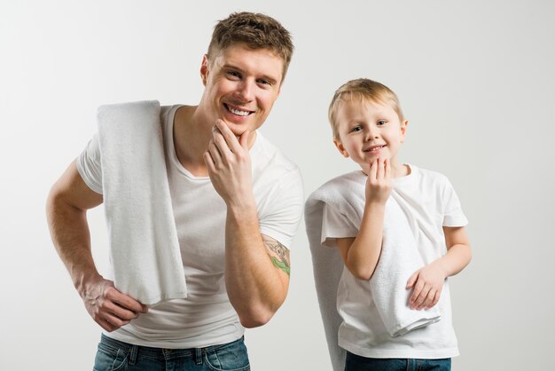 Close-up of father and son touching their chin with hands standing against white backdrop