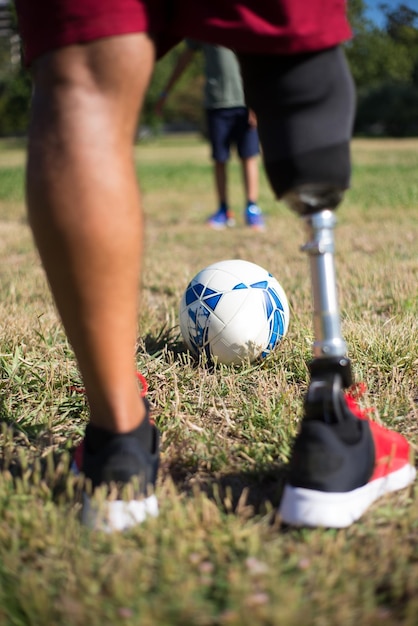 Foto gratuita primo piano del padre con la gamba protesica che gioca a calcio con il figlio. uomo con gamba meccanica in pantaloncini e ragazzino nel parco. disabilità, famiglia, concetto di amore