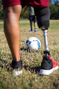 Close-up of father with prosthetic leg playing football with son. man with mechanical leg in shorts and little boy in park. disability, family, love concept