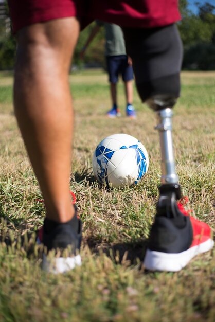 Close-up of father with prosthetic leg playing football with son. Man with mechanical leg in shorts and little boy in park. Disability, family, love concept