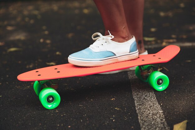 Close up of feet of girl sneakers rides on orange penny skateboard on asphalt
