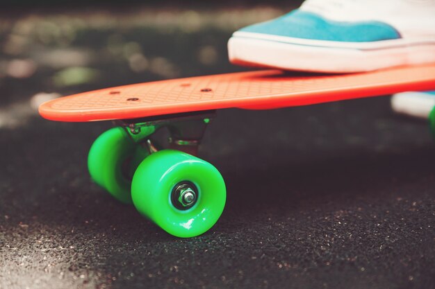 Close up of feet of girl sneakers rides on orange penny skateboard on asphalt