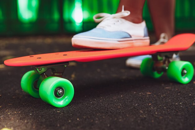 Close up of feet of girl sneakers rides on orange penny skateboard on asphalt