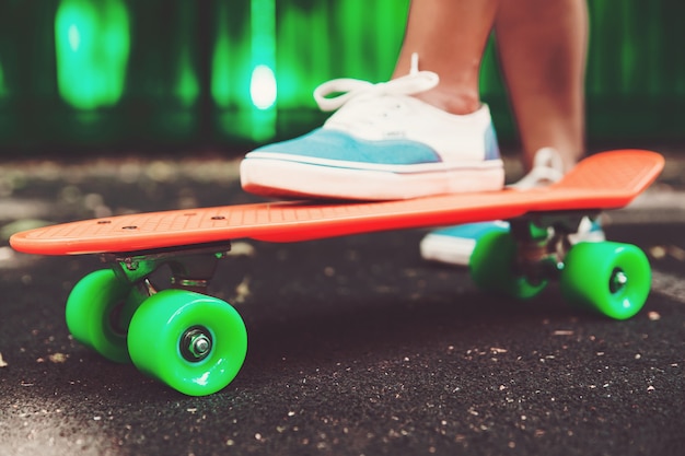 Close up of feet of girl sneakers rides on orange penny skateboard on asphalt