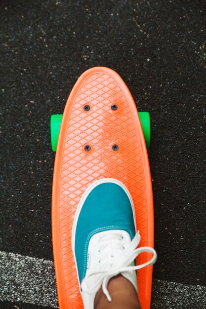 Close up of feet of girl sneakers rides on orange penny skateboard on asphalt