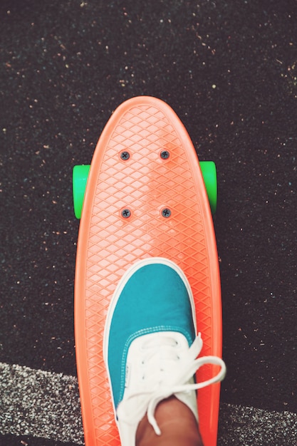 Free photo close up of feet of girl sneakers rides on orange penny skateboard on asphalt