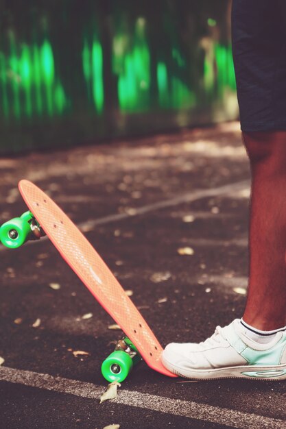 Close up of feet of man sneakers rides on orange penny skateboard on asphalt