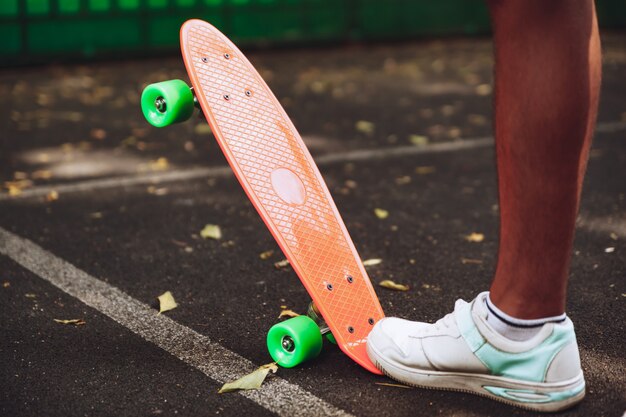 Close up of feet of man sneakers rides on orange penny skateboard on asphalt