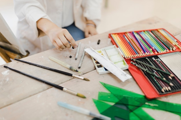 Close-up of female artist holding black crayons on wooden table