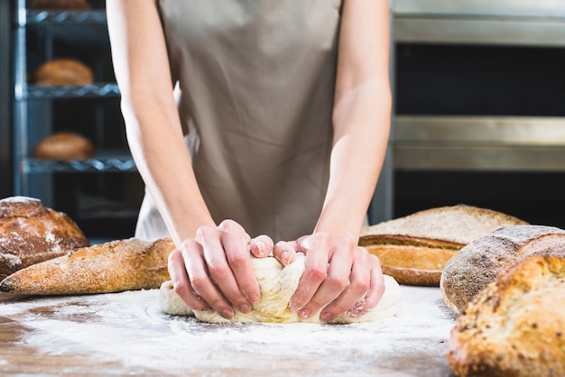 Close-up of female baker kneading the dough with flour on wooden surface