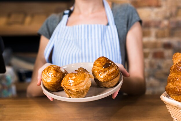 Close-up of female baker's hand showing baked sweet puff pastries at the counter