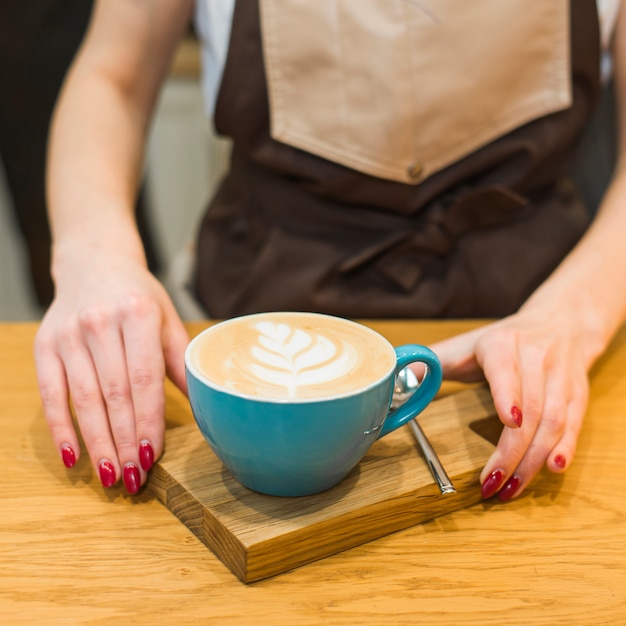 Close-up of female barista serving coffee on wooden chopping board at cafeteria