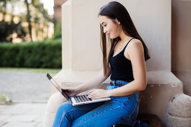 Chiuda su di uno studente di college femminile che si siede in un prato inglese facendo uso del suo computer portatile un giorno soleggiato.