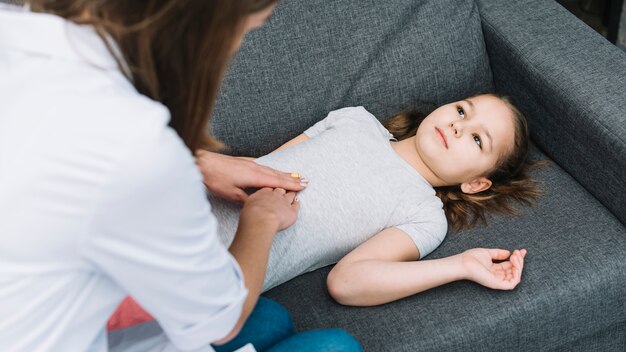 Close-up of female doctor examining patient girl lying on gray sofa