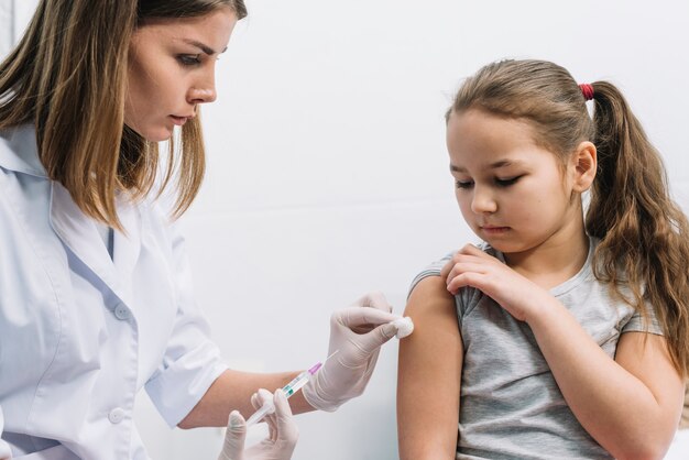 Close-up of female doctor injecting the syringe on patient's arm against white background