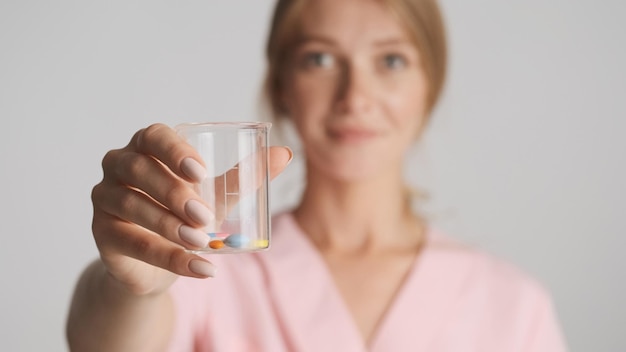 Close up female doctor offering medical pills on camera over white background