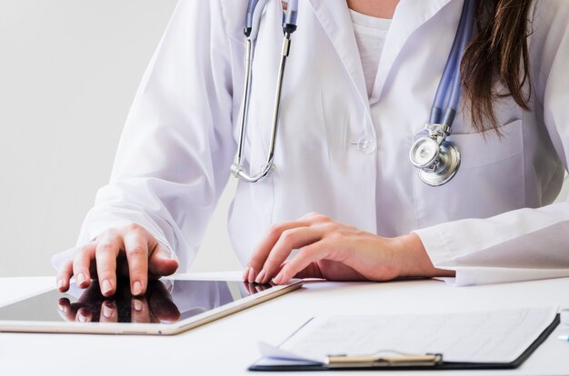 Close-up of a female doctor using digital tablet and medical report on desk