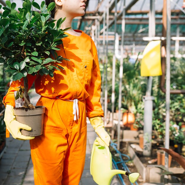 Close-up of a female gardener in workwear holding potted plant and watering can