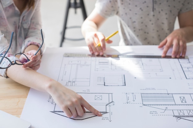 Close-up of female hand pointing on blueprint over table at workplace