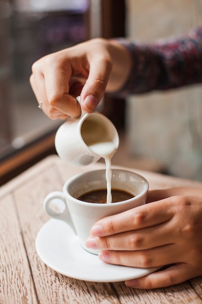 レストランでコーヒーカップに牛乳を注ぐ女性の手のクローズアップ