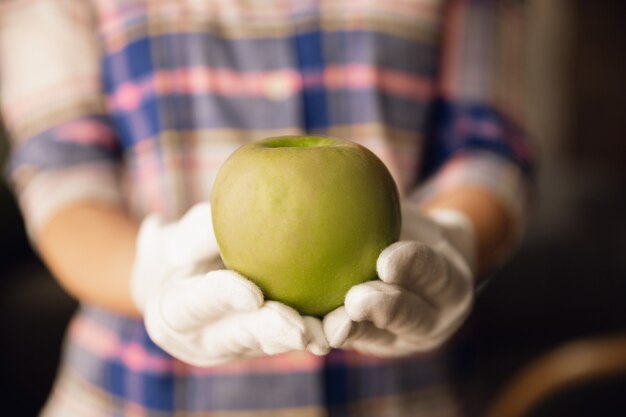 Close up of female hands in gloves holding green apple, healthy food, fruits. Diet organic nutrition, natural and fresh product full of vitamins. Preparing, proposing for somebody. Copyspace.