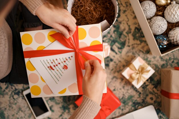 Close up female hands tying a red ribbon bow on a craft gift box.