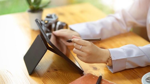 Крупным планом женские руки с помощью стилуса, рисунок на экране портативного цифрового планшета на рабочем столе.