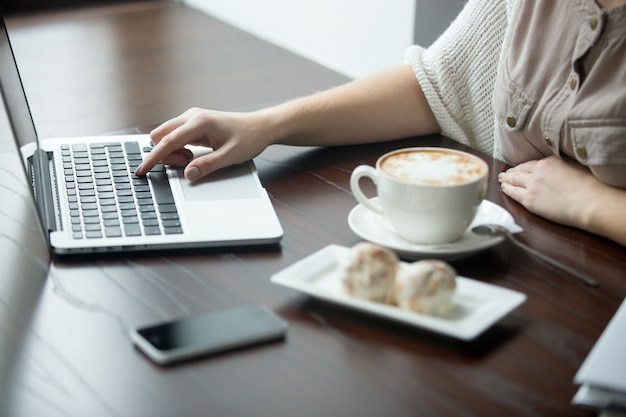 カフェ、ノートパソコンで働く女性の手のクローズアップ