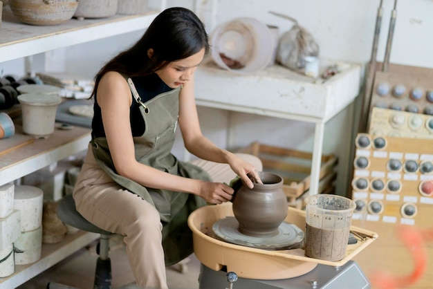 ろくろに取り組んでいる女性の手のクローズアップホームスタジオワークショップアートと作成趣味のコンセプトでろくろに金型小さな花瓶ボウル粘土を形作るアジアの女性の彫刻の女性