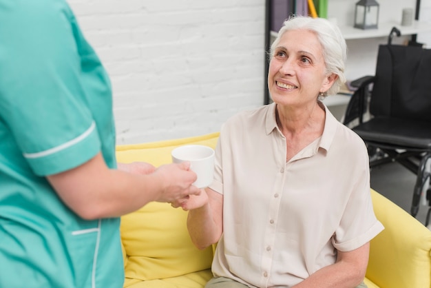 Close-up of female nurse serving coffee to senior woman