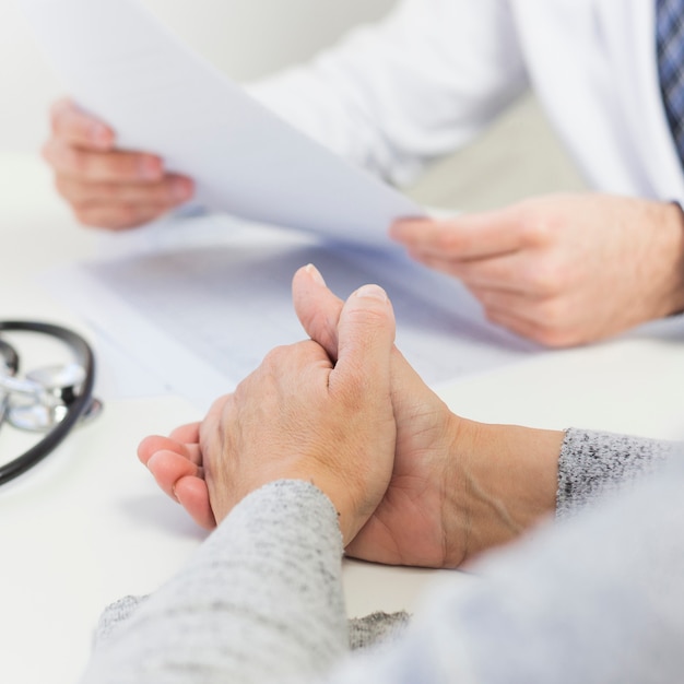 Close-up of female patient sitting near the doctor holding medical report