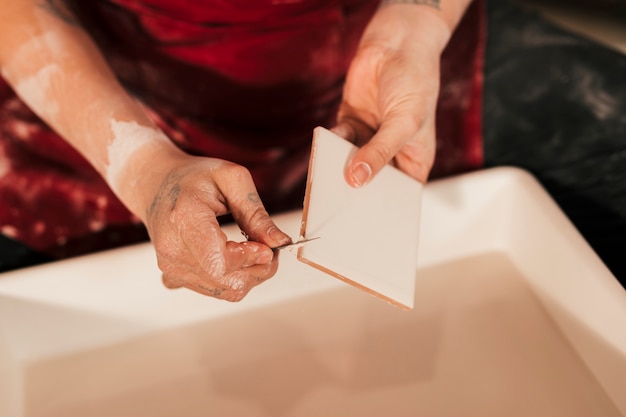 Close-up of female potter carving the white tiles with tools