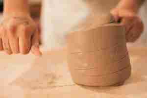 Free photo close-up of female potter's hand cutting the clay with thread on table