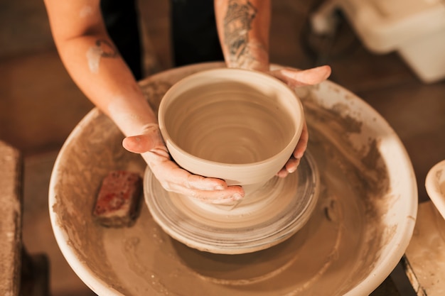 陶器のホイール上の粘土のボウルに形を与える女性の陶工の手のクローズアップ