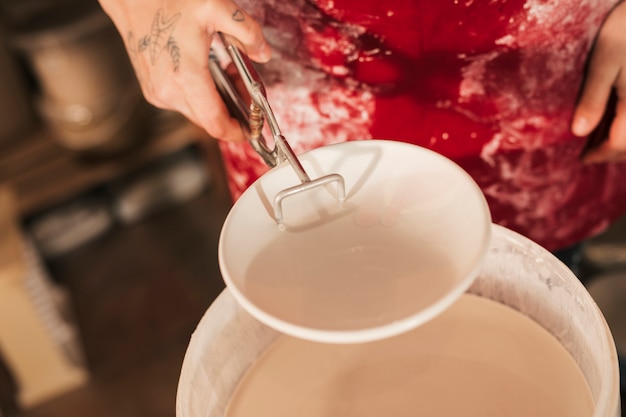 トングで塗られたセラミックプレートを持っている女性の陶工の手のクローズアップ