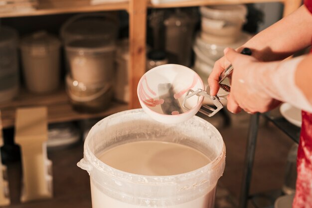 Close-up of female potter's hand inserting the bowl in paint bucket with tong